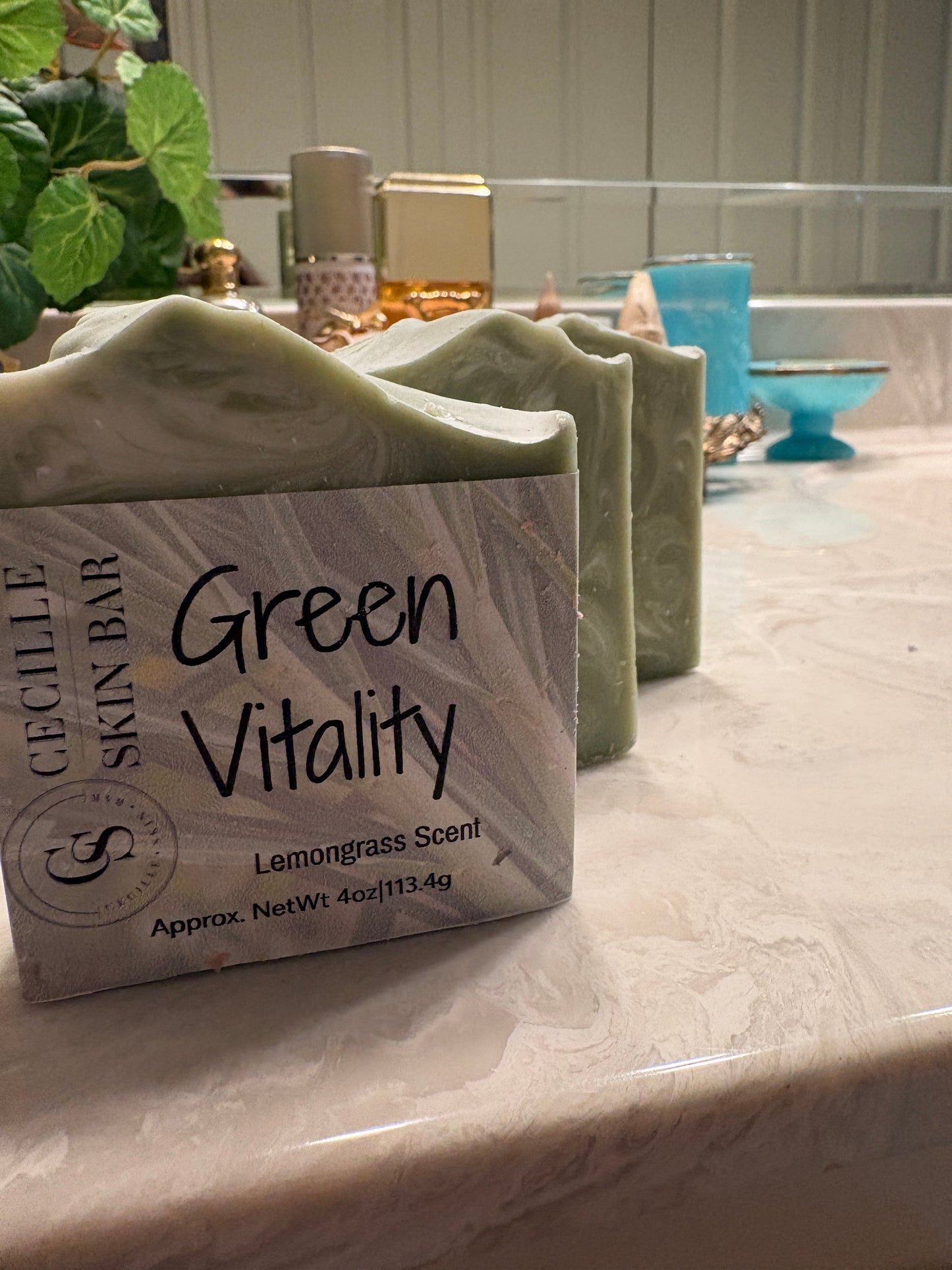 A bar of Cécile Skin Bar soap labeled 'Green Vitality' sits on a marble countertop in a bathroom setting, with other bars and toiletries blurred in the background.