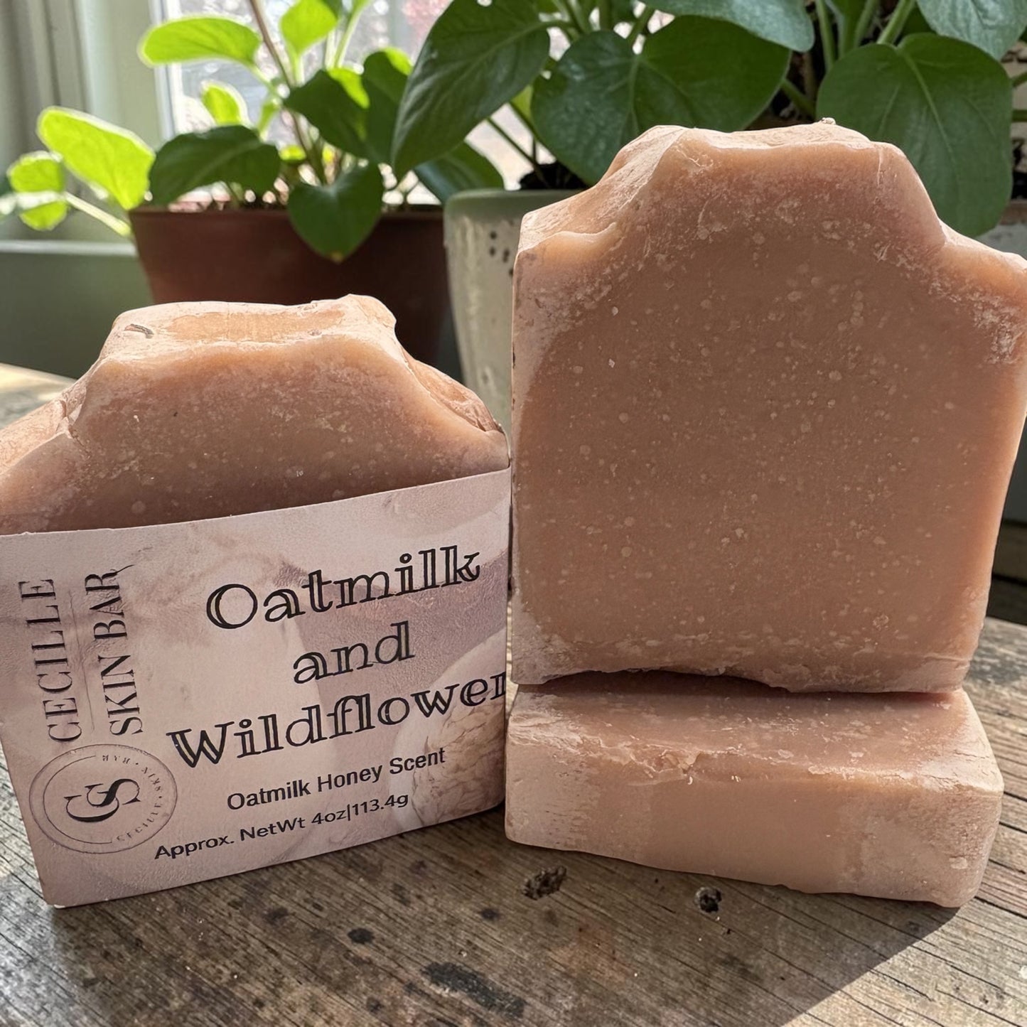 Two rough-cut natural soap bars in a dusty peach-pink color are displayed on a rustic wooden table. One bar is standing upright and stacked with another bar in front.